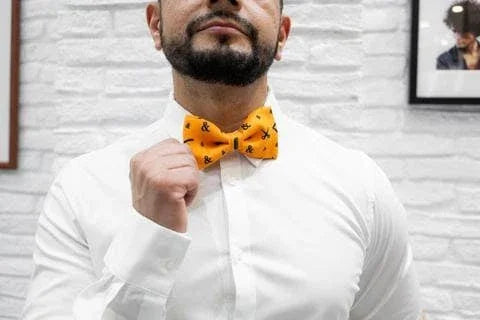 Hombre con pajarita amarilla con diseños negros ajustándose la corbata en boda