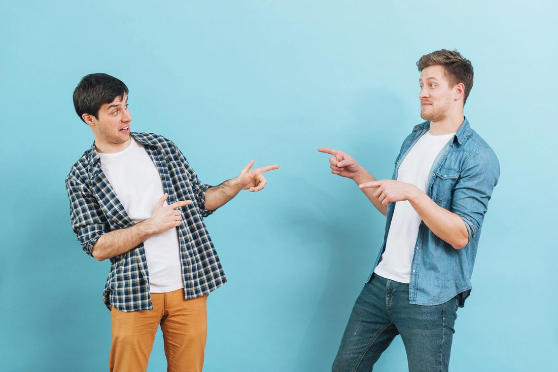 Dos hombres jóvenes señalándose mutuamente con camisetas blancas y camisas casuales frente a fondo azul