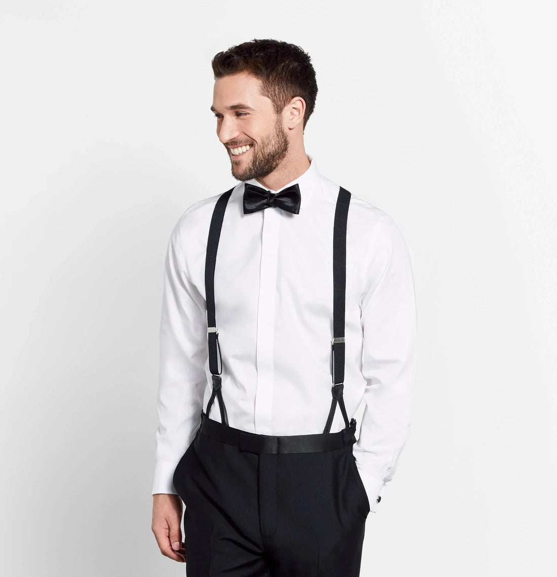 Hombre sonriente con camisa blanca, tirantes y pajarita negra, estilo elegante y formal