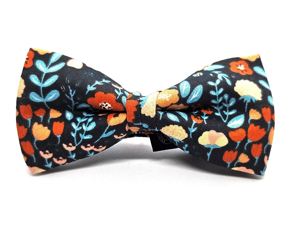 Pajarita de tela negra con diseño floral en tonos naranjas, azules y beige, hecha a mano