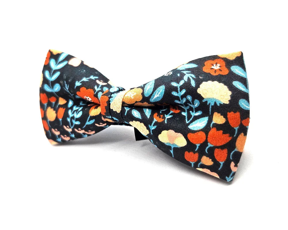 Pajarita con estampado floral naranja, azul y beige sobre fondo negro, complemento original y artesanal